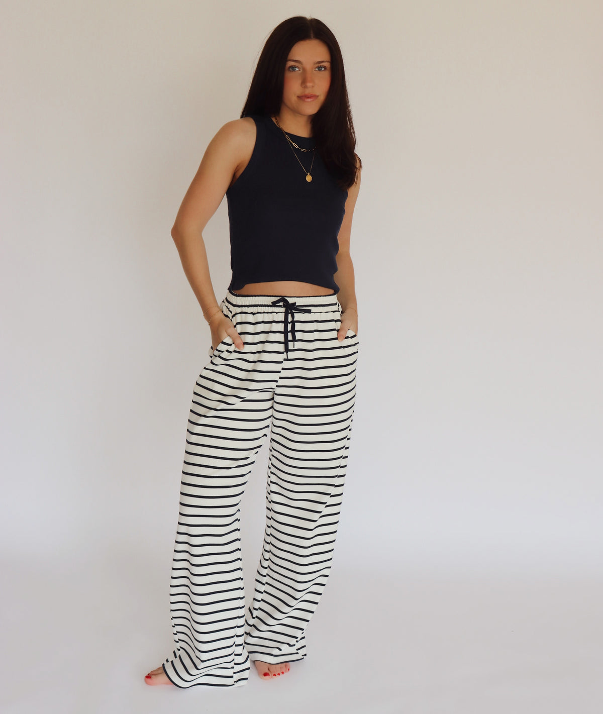 Woman wearing a navy blue sleeveless top and striped pants against a plain background