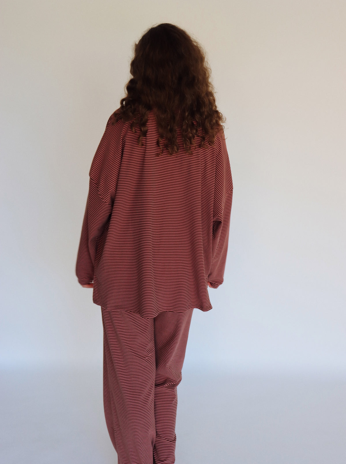 A woman modeling a matching two-piece loungewear set consisting of a long-sleeve top and pants, both featuring thin horizontal stripes in a pink and dark brown colorway.