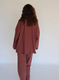 A woman modeling a matching two-piece loungewear set consisting of a long-sleeve top and pants, both featuring thin horizontal stripes in a pink and dark brown colorway.