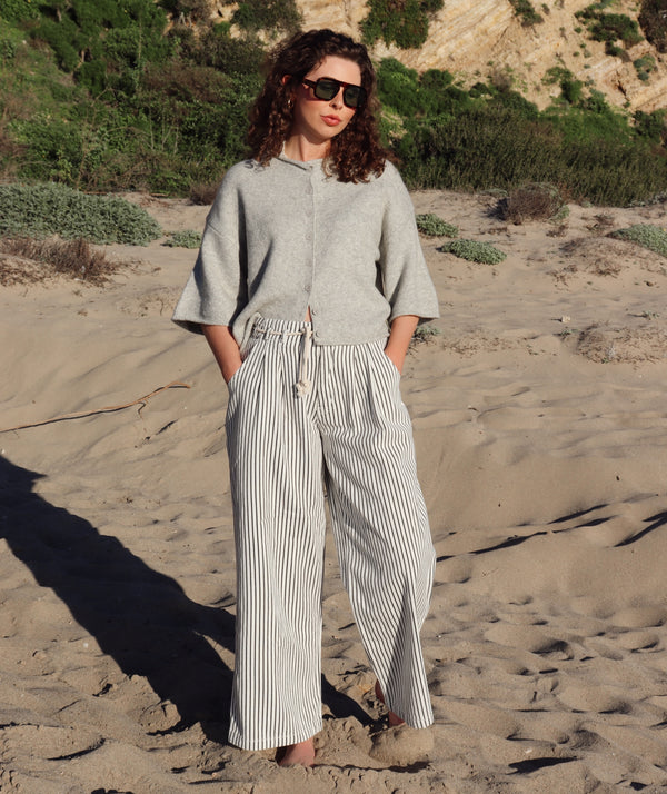 Person wearing a gray top and striped pants standing on a sandy beach.