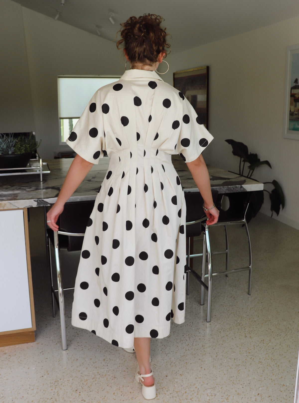 Woman in a polka dot dress walking in a modern kitchen.