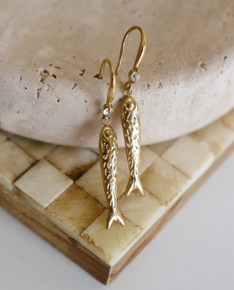 Gold fish-shaped earrings on a stone surface