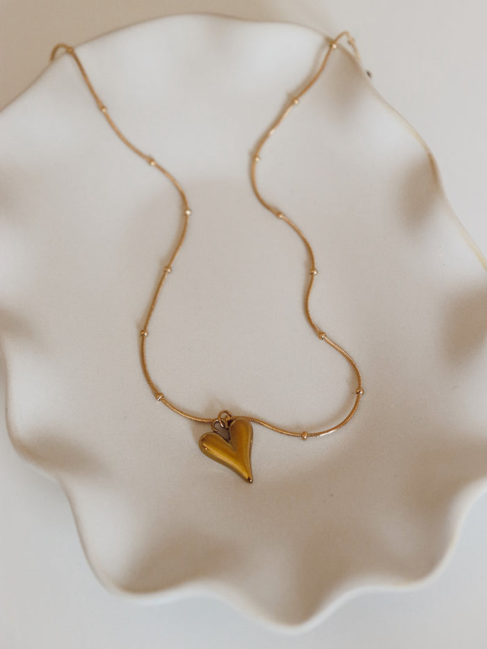Gold necklace with a heart-shaped pendant on a white surface