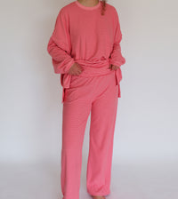 A person wearing a matching pink striped lounge set, consisting of a long-sleeve top and wide-leg pants, standing against a plain white background.