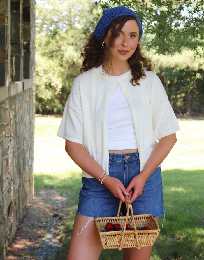Woman holding a woven basket outdoors with a stone building and greenery in the background