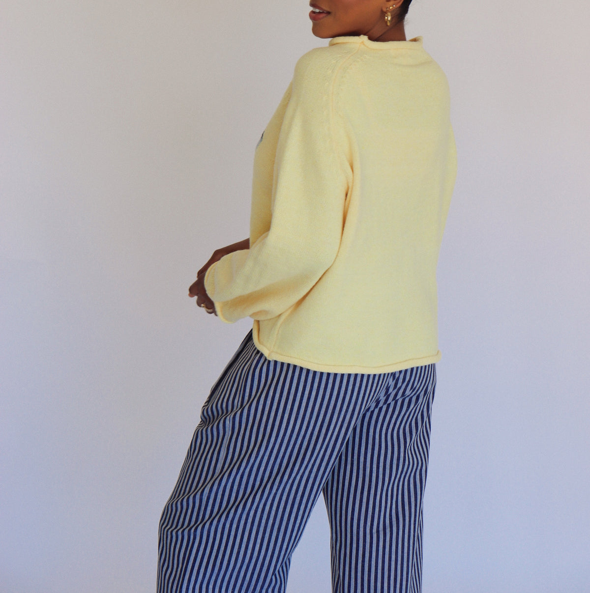 Person wearing a light yellow sweater and striped pants against a plain background
