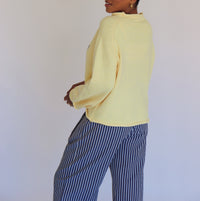 Person wearing a light yellow sweater and striped pants against a plain background