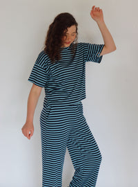A woman modeling a matching two-piece loungewear set consisting of a short-sleeve crewneck top and wide-leg pants, both featuring horizontal dark teal and navy stripes.