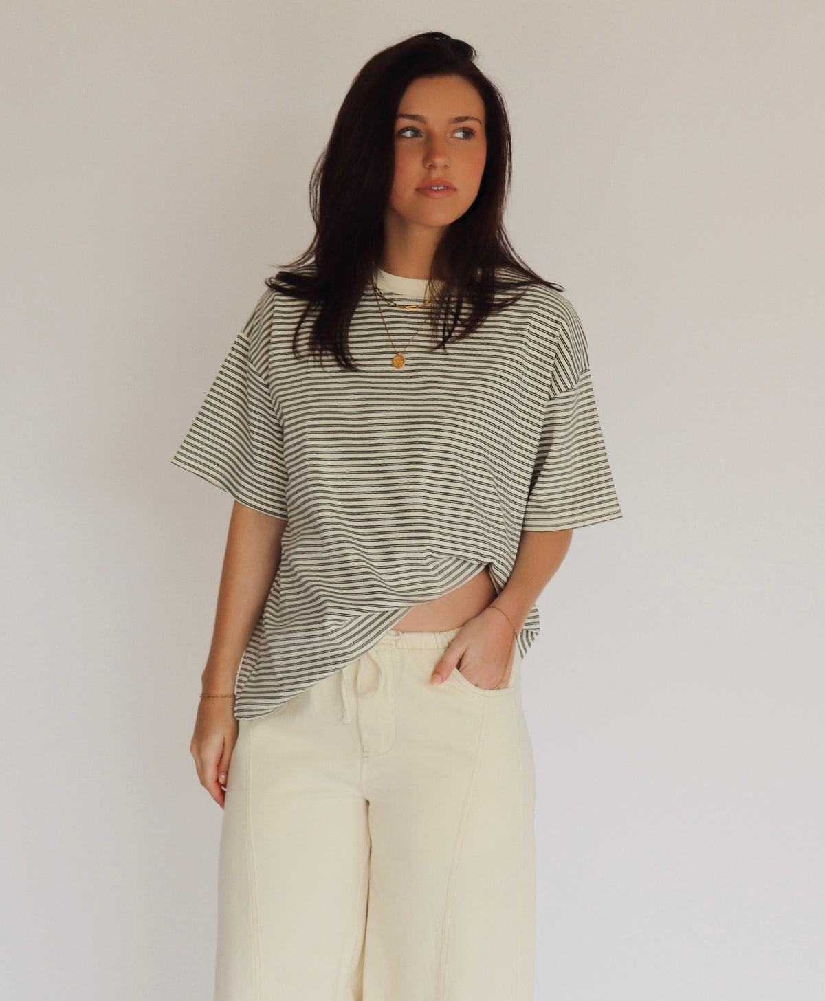 Woman wearing a striped shirt and cream pants against a plain background