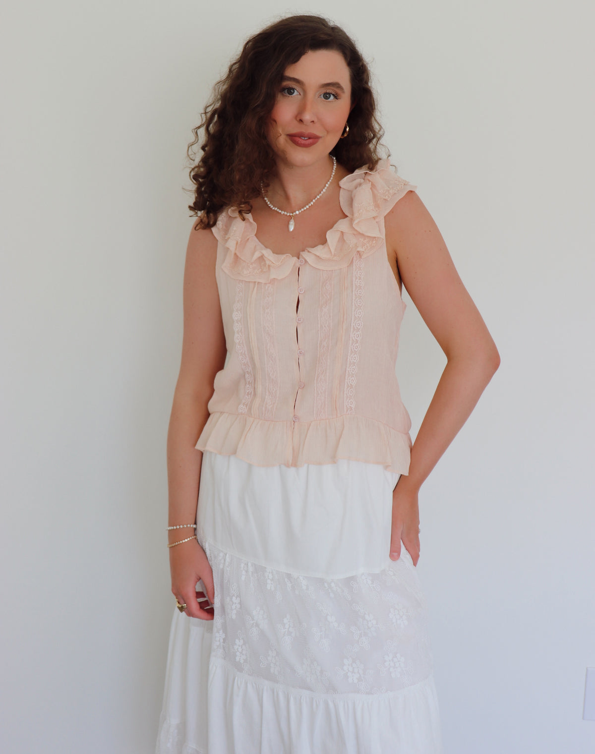 Woman wearing a light pink blouse with ruffled neckline against a plain background