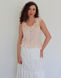 Woman wearing a light pink blouse with ruffled neckline against a plain background