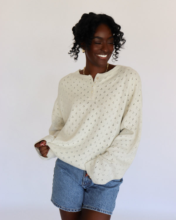 Woman wearing a cream/light gray sweater with small pointelle patterns and denim shorts on a white background