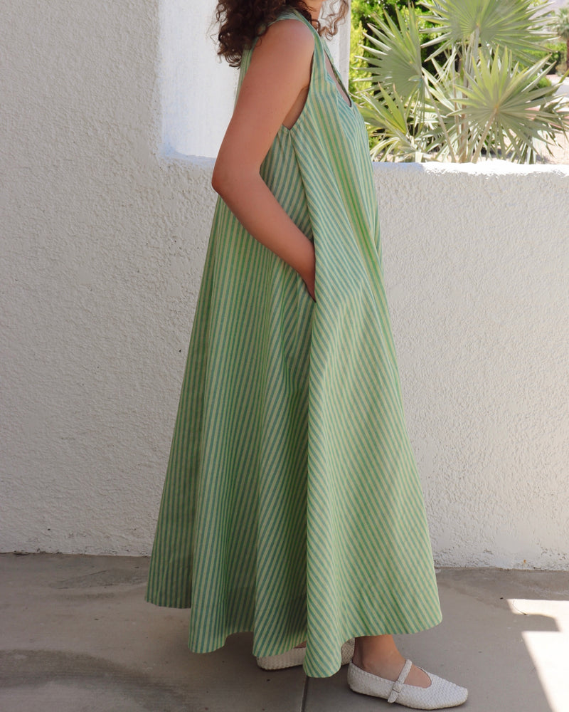 Woman wearing a green striped dress standing against a white wall with plants in the background.