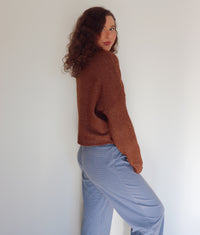Woman wearing a brown cardigan over blue and brown striped pants against a plain background.