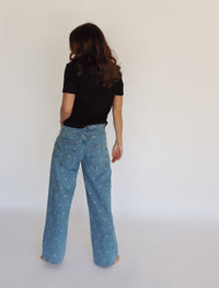 A woman modeling a black short-sleeve top and light blue wide-leg denim jeans with small white polka dots, standing against a plain white studio background.