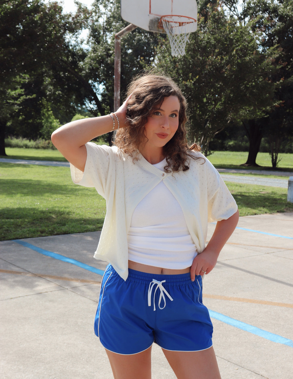 Woman standing on a basketball court wearing a white top and blue shorts.