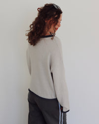 Person wearing a light gray sweater and dark pants against a white background