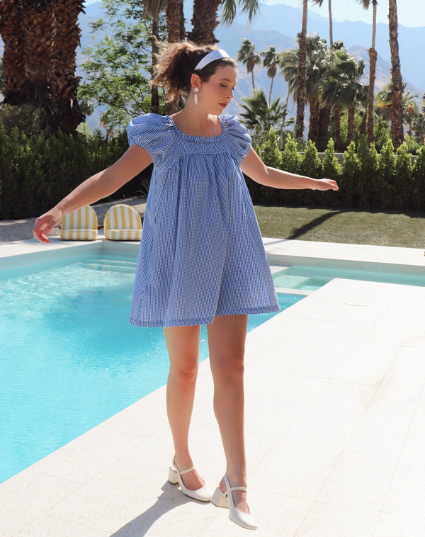 Woman in a blue dress standing by a pool with palm trees in the background