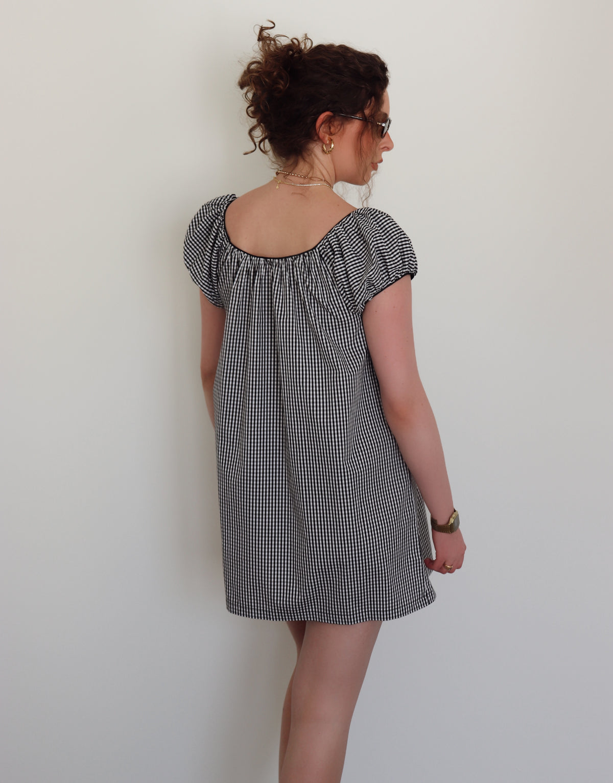 Woman wearing a black and white checkered dress against a white wall.