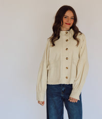 Woman wearing a beige jacket with buttons against a plain background