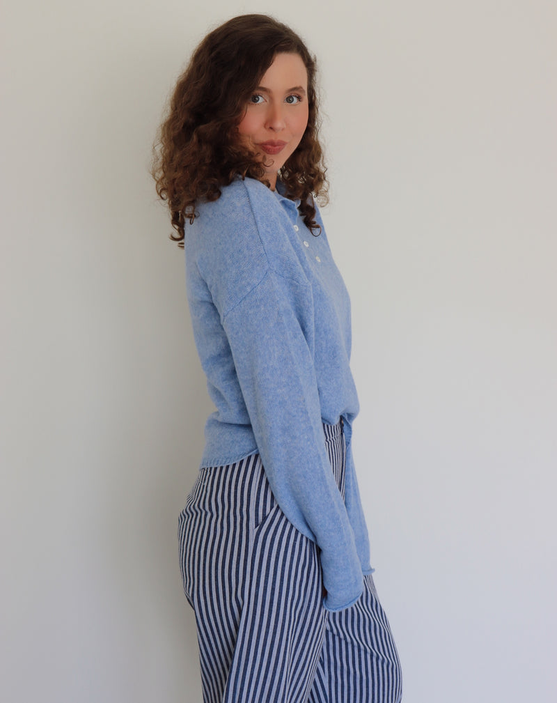 Person wearing a blue henley and striped pants against a plain background