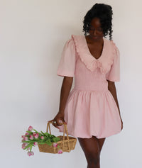 Woman wearing a pink dress holding a basket of flowers against a white background
