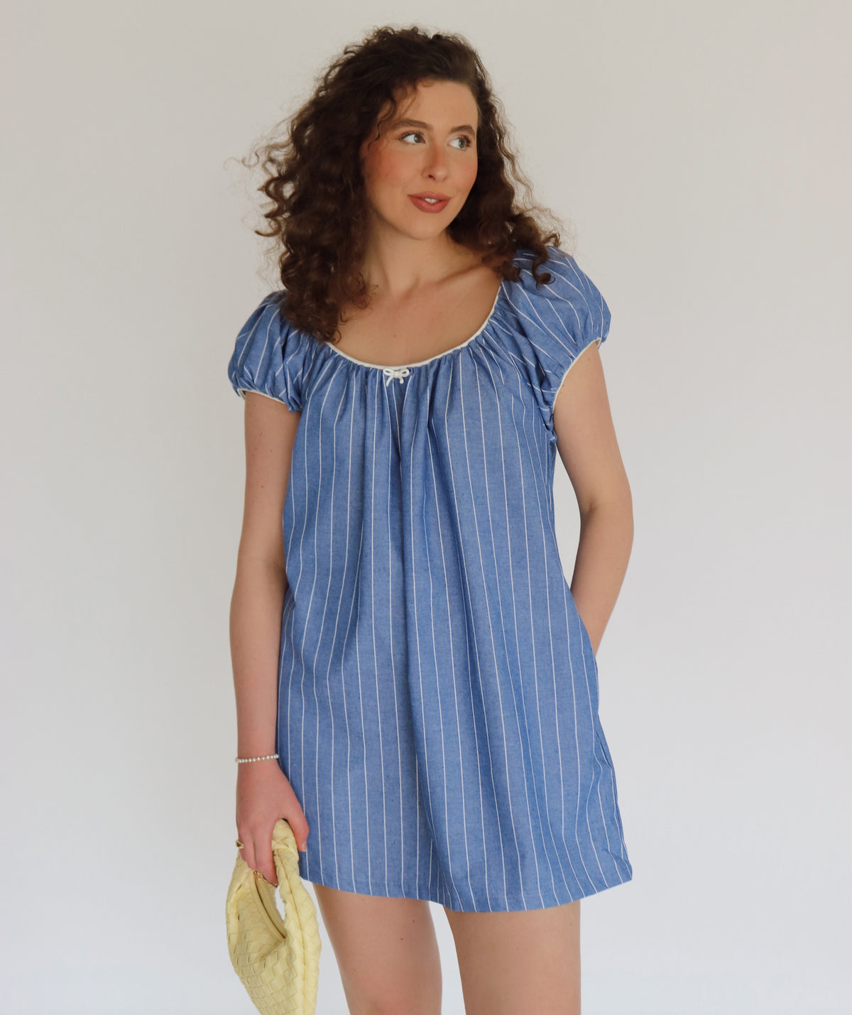 Woman wearing a blue striped dress holding a yellow bag against a plain background