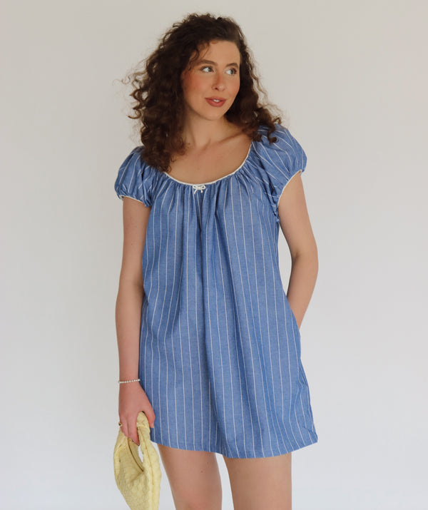 Woman wearing a blue striped dress holding a yellow bag against a plain background