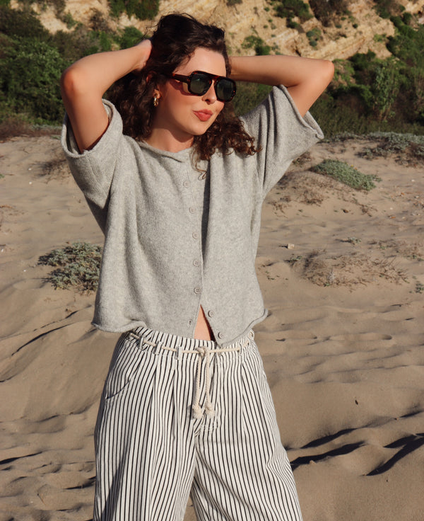 Person wearing a gray top and striped pants standing on a sandy beach.