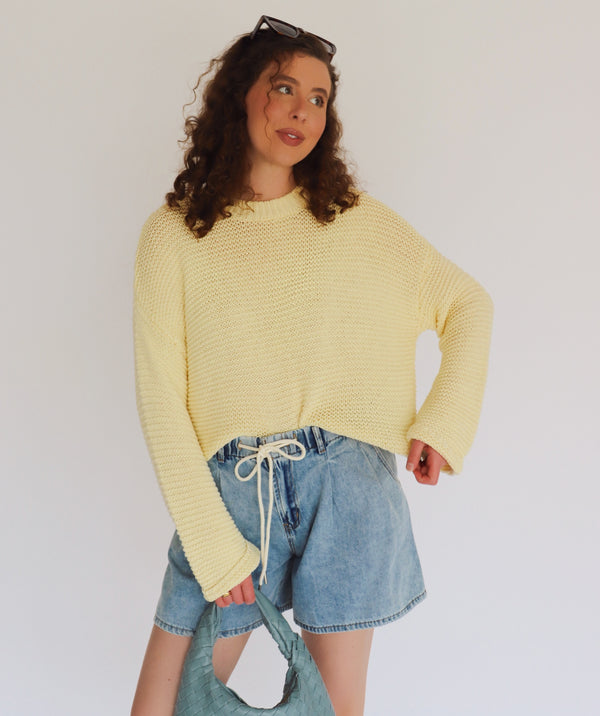 Person wearing a yellow sweater and denim shorts against a plain background