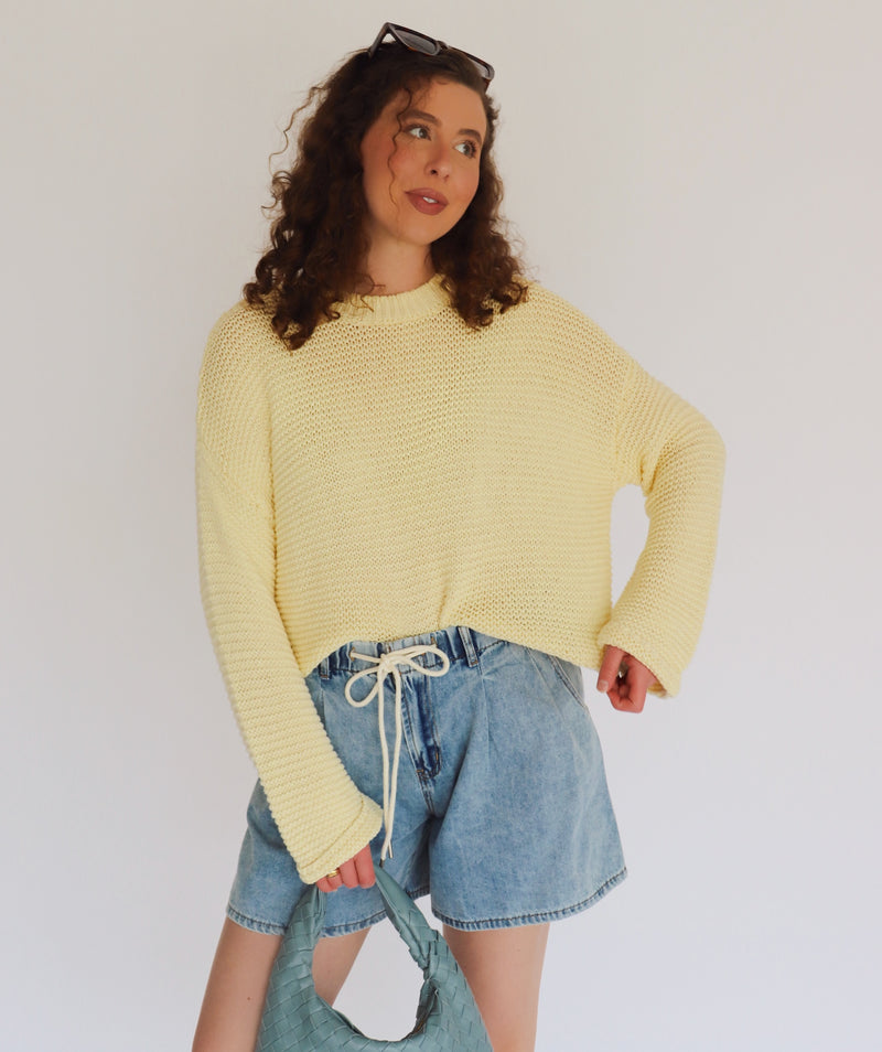 Person wearing a yellow sweater and denim shorts against a plain background