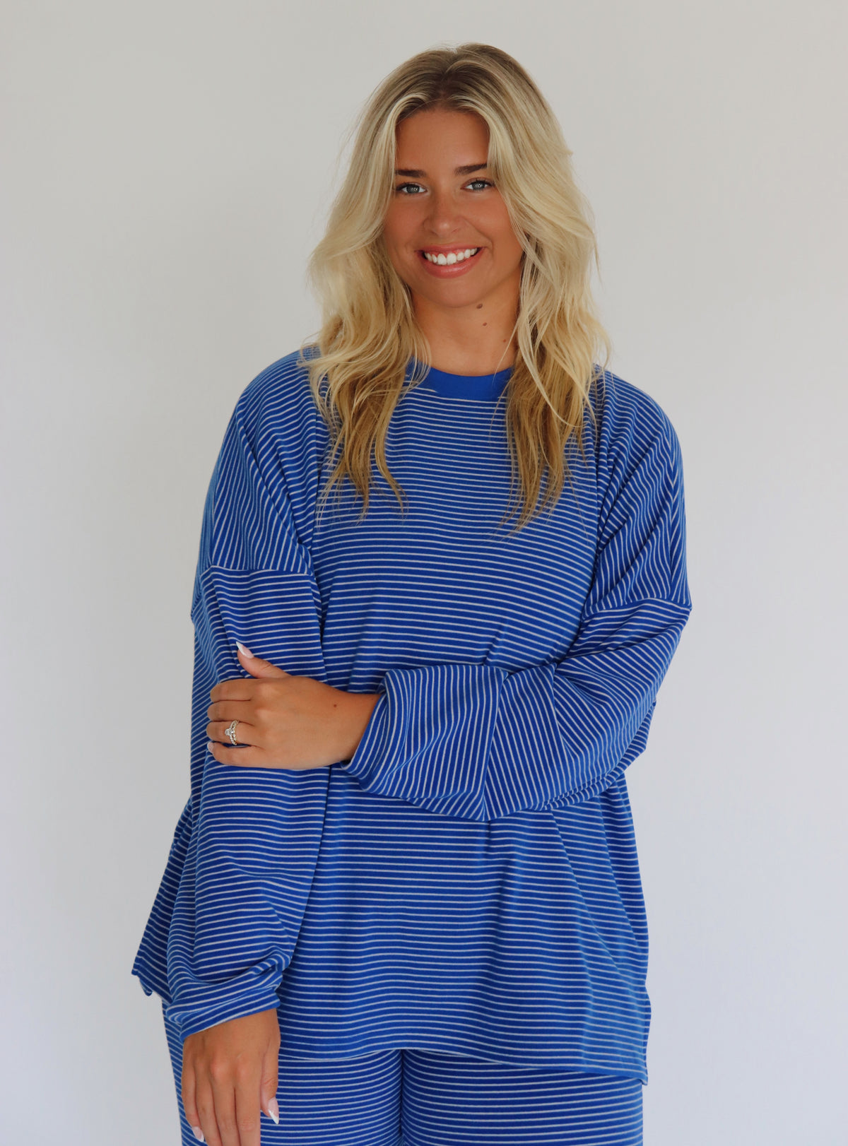 A woman modeling a matching blue striped lounge set consisting of a long-sleeve top and pants,  standing against a plain white studio background.