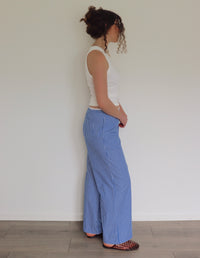 Woman wearing a white top and blue striped pants against a plain wall.