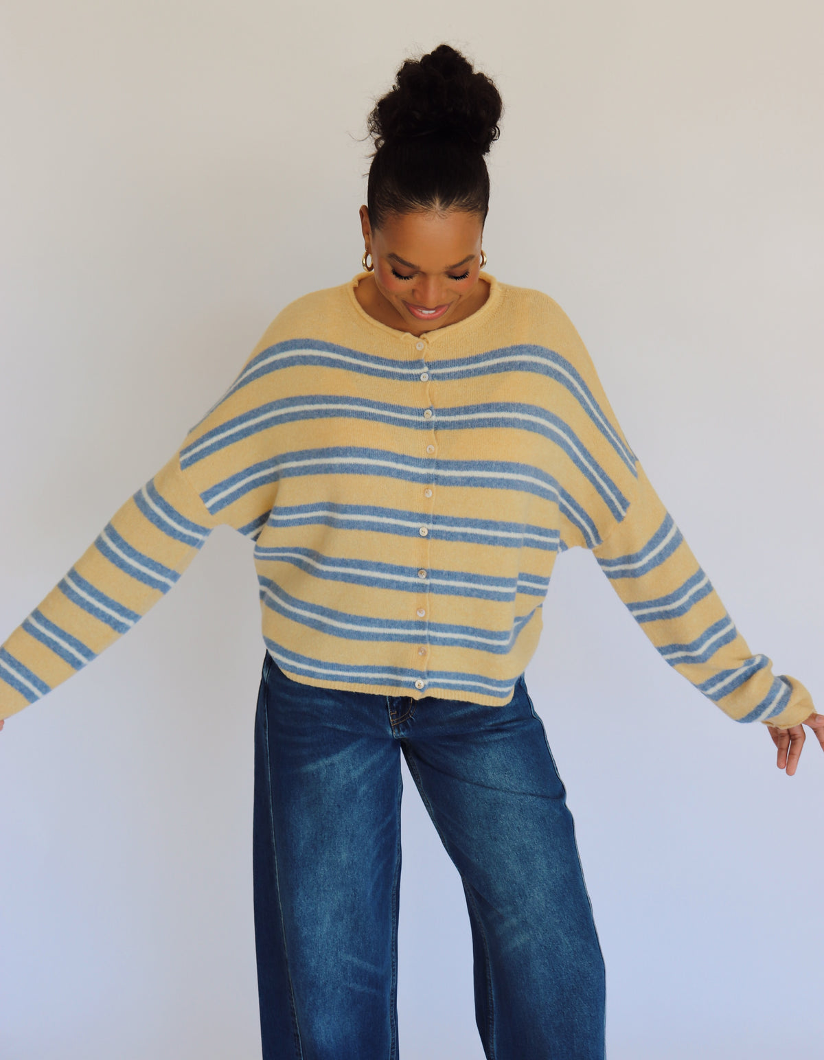Person wearing a yellow and blue striped cardigan and blue jeans against a white background