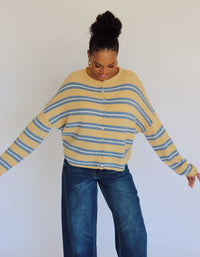 Person wearing a yellow and blue striped cardigan and blue jeans against a white background