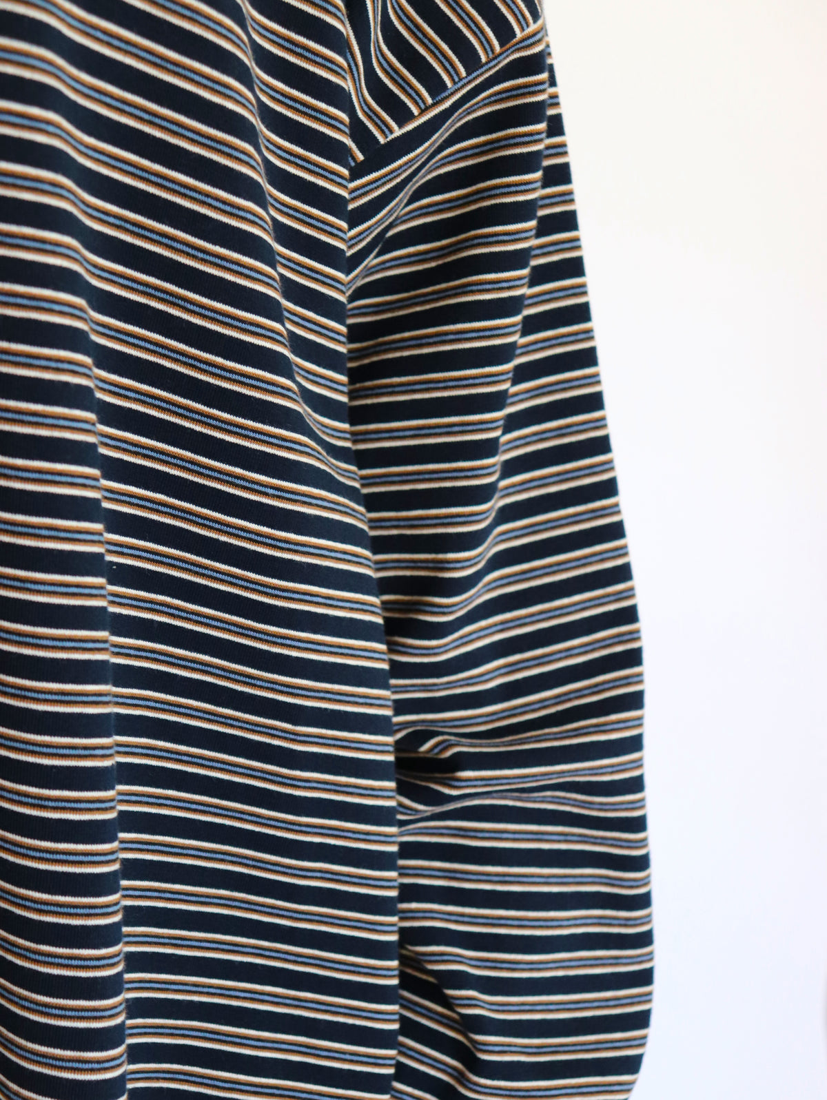 Close-up of a striped long-sleeve top or dress fabric, featuring horizontal navy blue, beige, and white stripes against a plain white background.