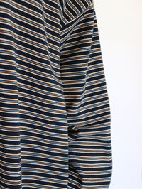 Close-up of a striped long-sleeve top or dress fabric, featuring horizontal navy blue, beige, and white stripes against a plain white background.