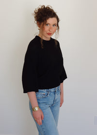 Person wearing a black top and blue jeans against a plain background