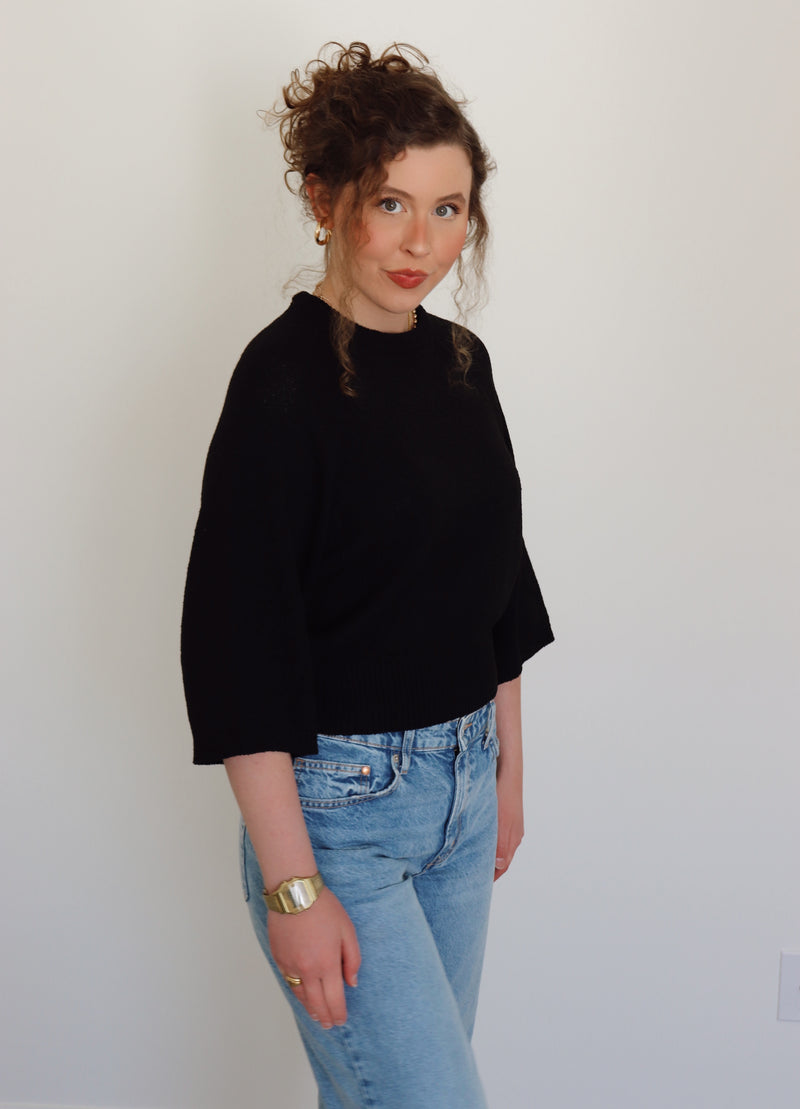 Person wearing a black top and blue jeans against a plain background