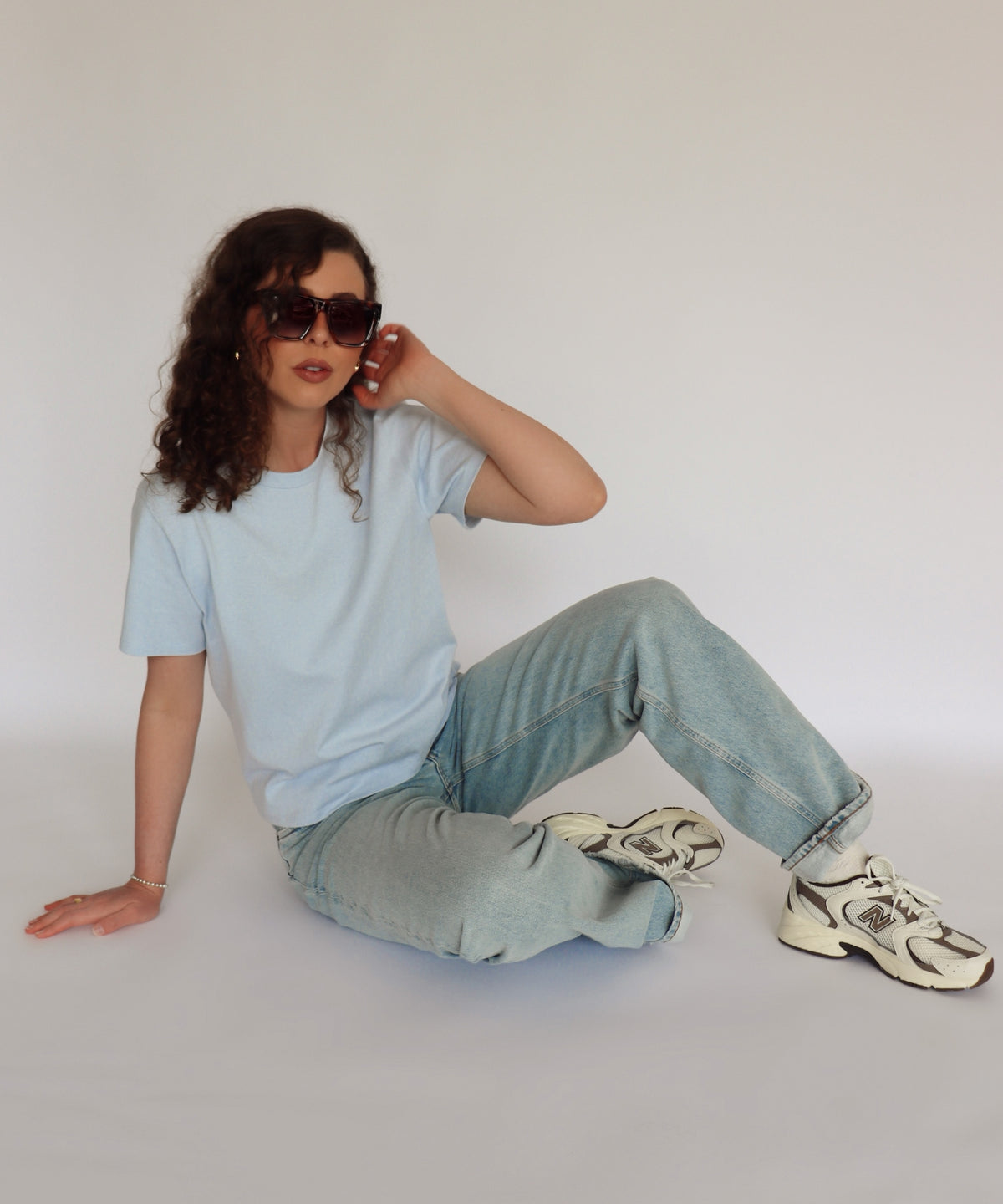 Woman wearing a light blue tee shirt and denim in front of a white background 