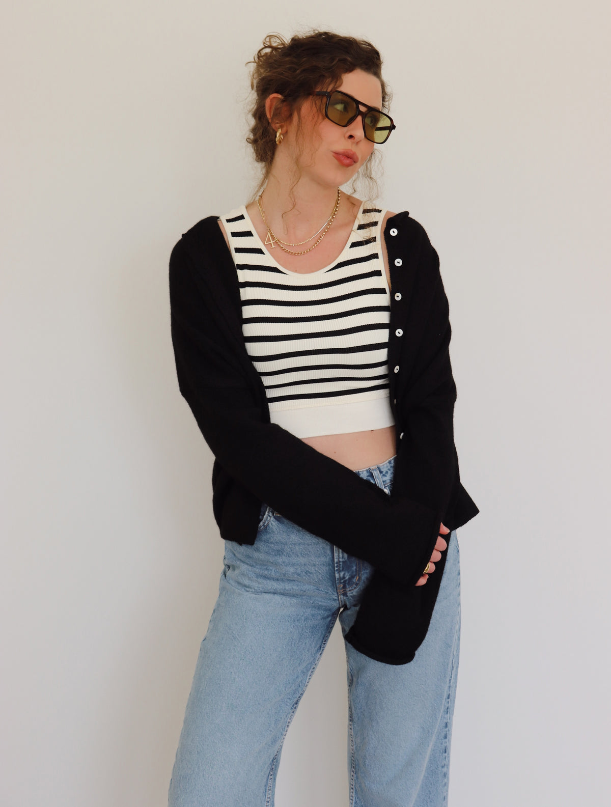Person wearing a black cardigan, striped top, and jeans against a plain background