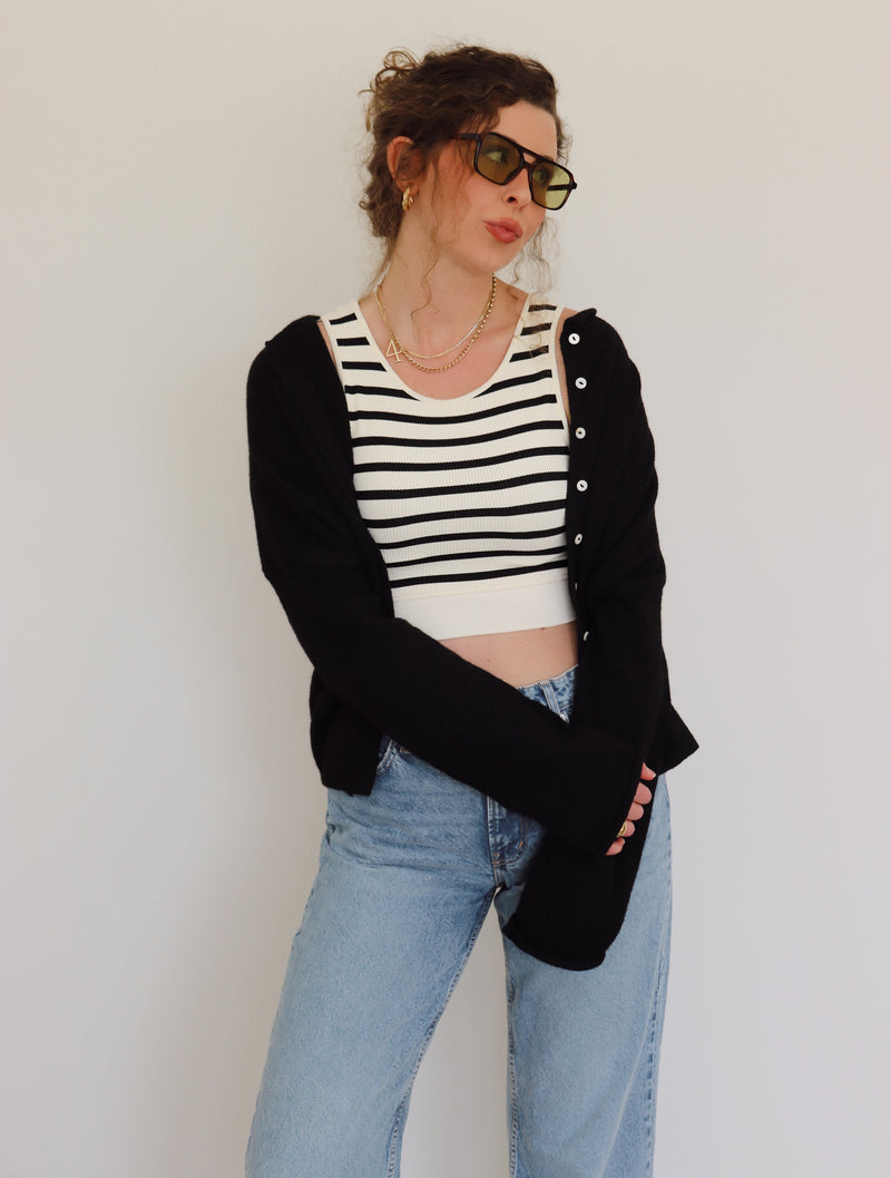 Person wearing a black cardigan, striped top, and jeans against a plain background