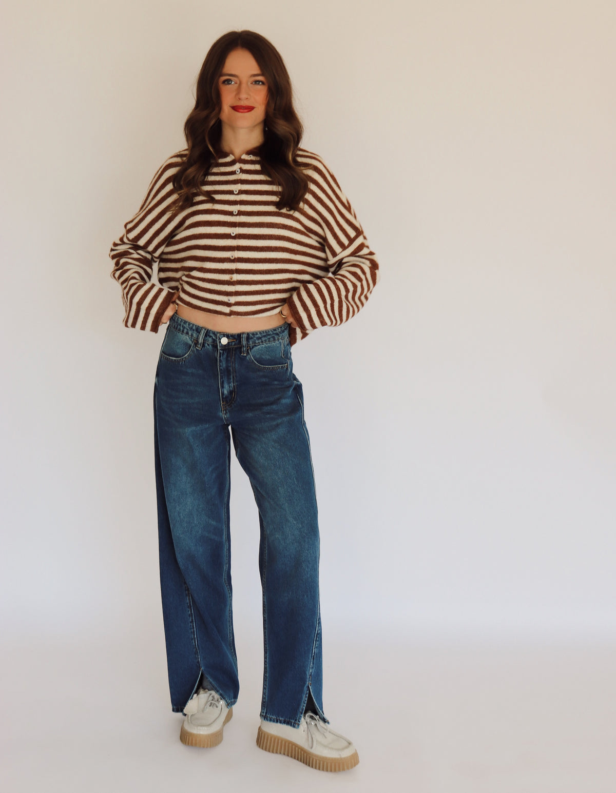 Woman wearing a brown and white striped sweater cardigan and blue jeans in front of  a white background