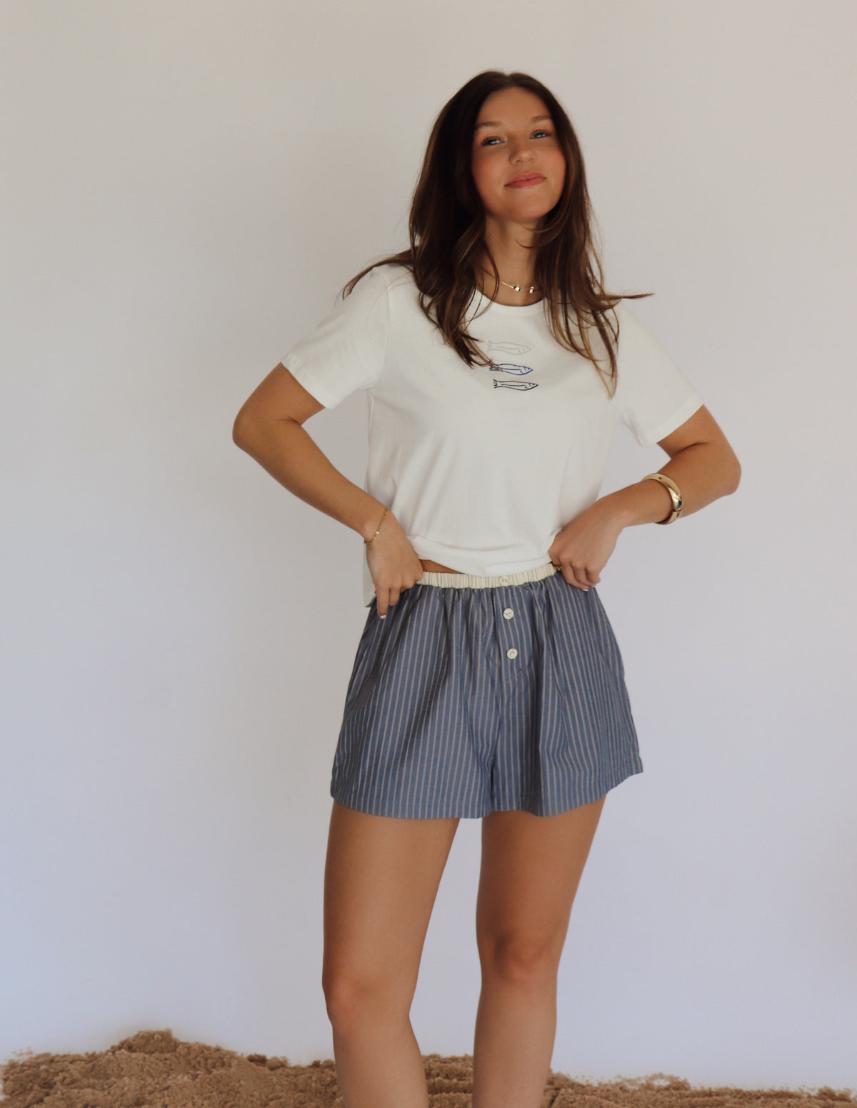 Woman wearing a white t-shirt and blue striped shorts against a plain background