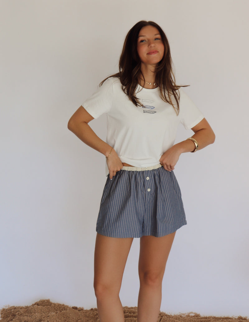 Woman wearing a white t-shirt and blue striped shorts against a plain background