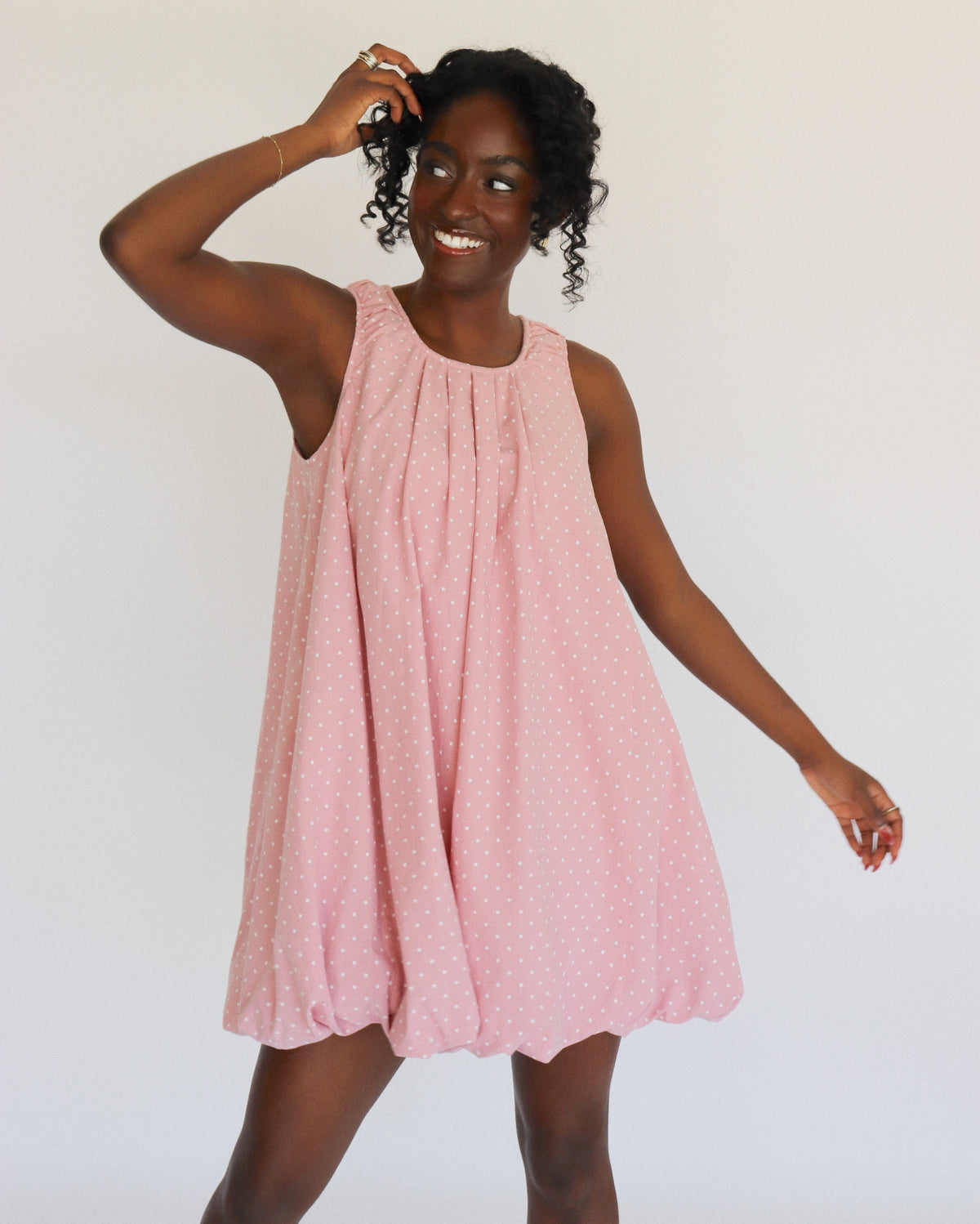 Woman wearing a pink dress with white polka dots on it against a white background