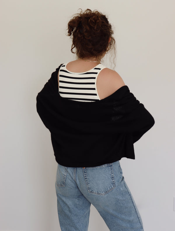 Person wearing a black oversized sweater over a striped top with light blue jeans against a plain background