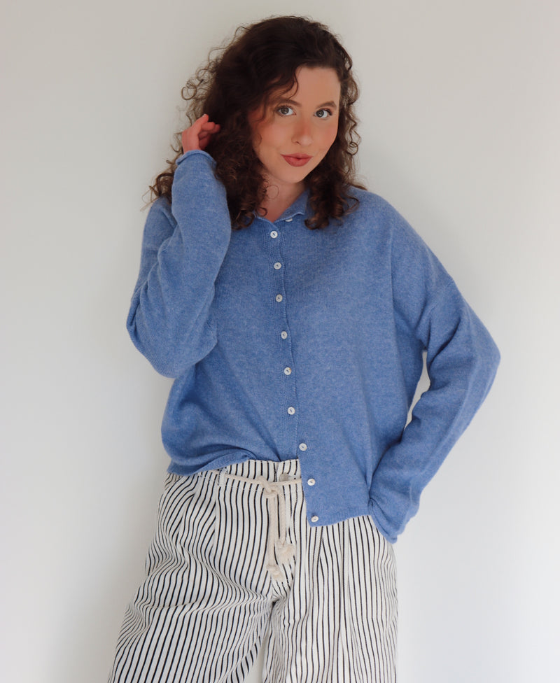 Woman wearing a blue cardigan and striped pants in front of a white wall.