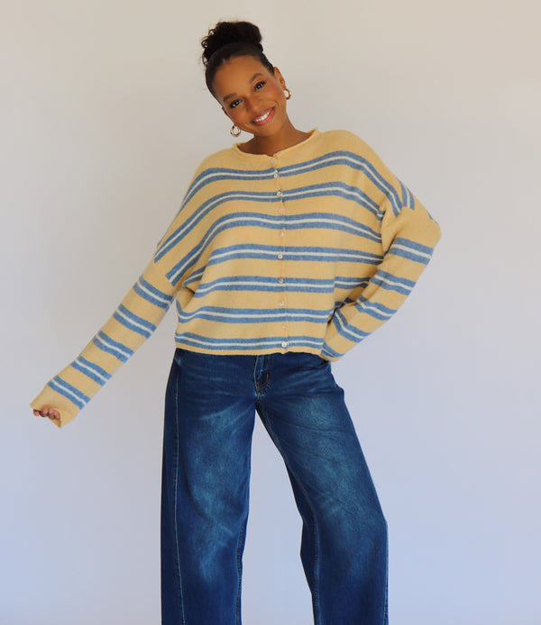 Person wearing a yellow and blue striped cardigan and blue jeans against a white background