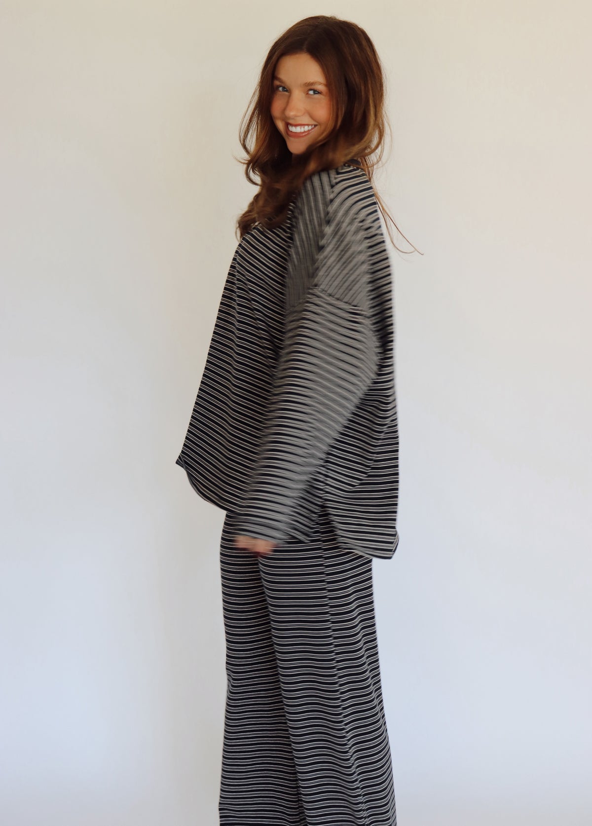 A woman modeling a matching two-piece loungewear set consisting of a long-sleeve top and wide-leg pants, both featuring a navy and white horizontal stripe pattern, set against a plain white studio background.